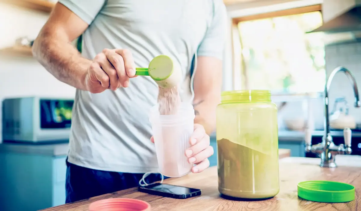 man adding protein powder into smoothie